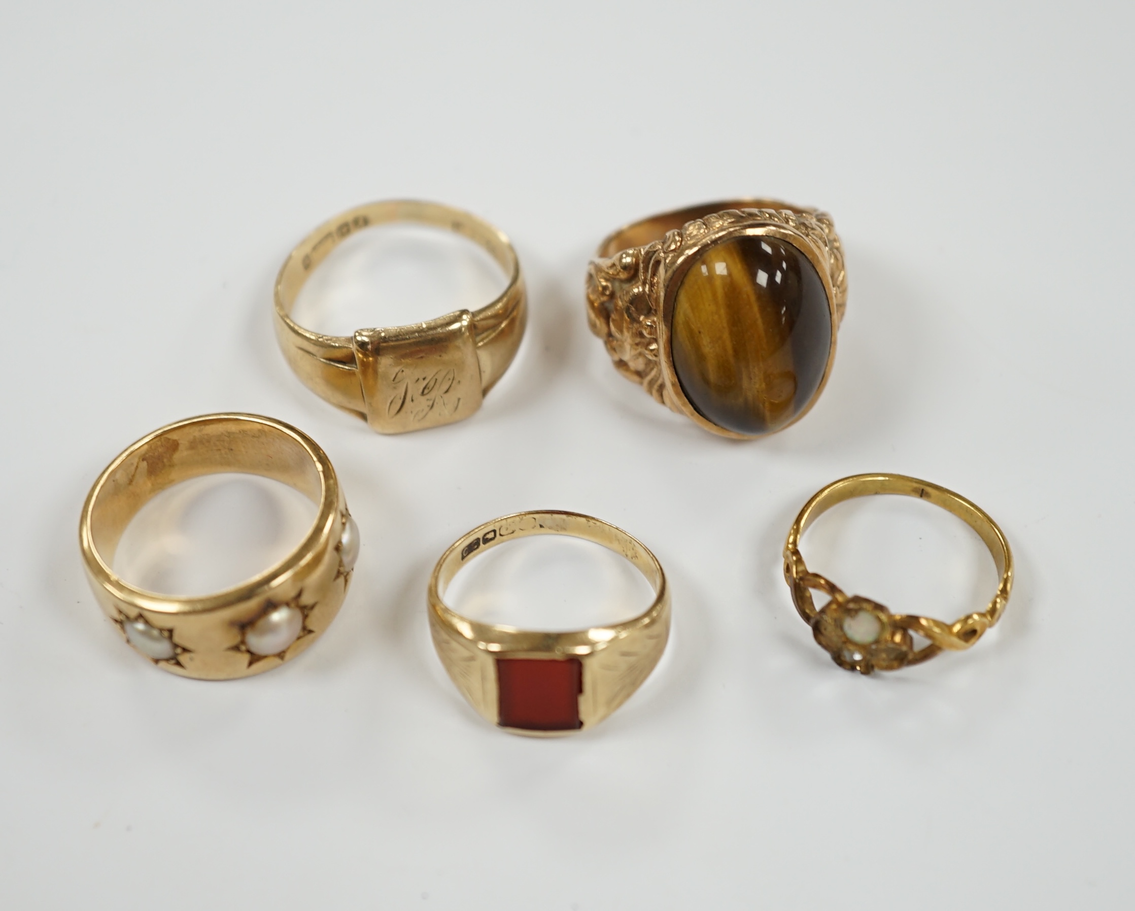 A 9ct gold signet ring, a gold and carnelian set signet ring and three yellow metal rings one set with three split pearls and one set with tiger's eye quartz cabochon, gross weight 29.7 grams.